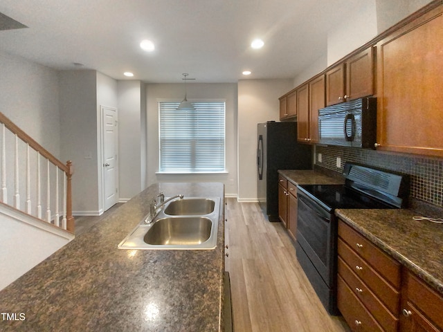 kitchen with light wood-type flooring, tasteful backsplash, sink, black appliances, and decorative light fixtures