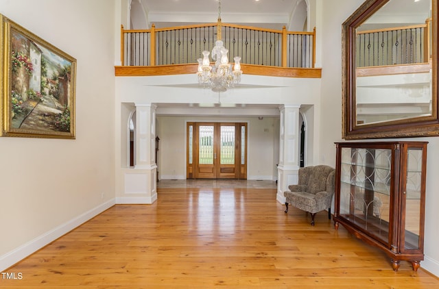 foyer with decorative columns, crown molding, light hardwood / wood-style flooring, and a towering ceiling