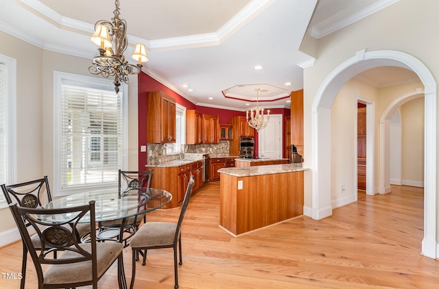 kitchen with backsplash, ornamental molding, a tray ceiling, light hardwood / wood-style flooring, and a chandelier
