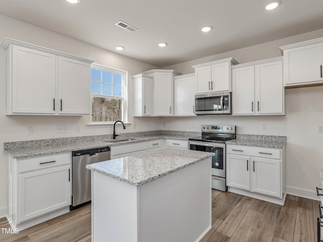 kitchen with light hardwood / wood-style floors, stainless steel appliances, a center island, sink, and white cabinetry