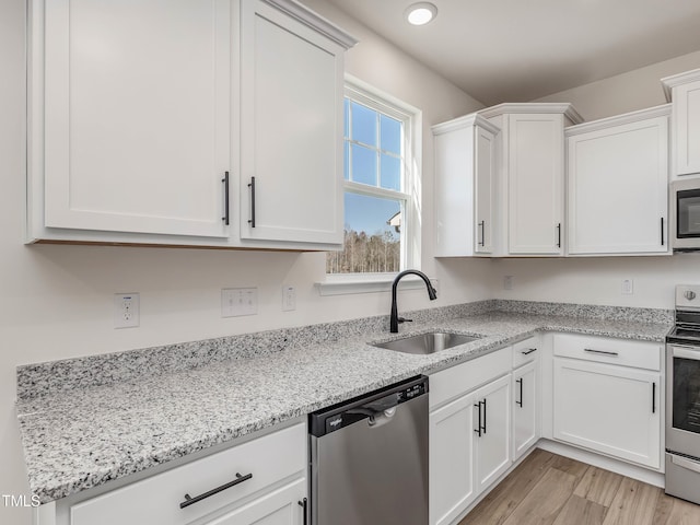 kitchen with a sink, stainless steel appliances, white cabinets, and light stone countertops