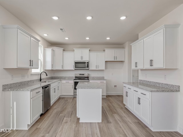 kitchen with stainless steel appliances, a kitchen island, white cabinetry, sink, and light hardwood / wood-style floors