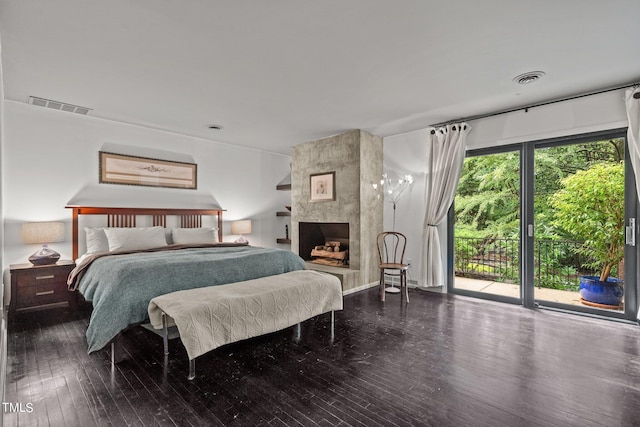 bedroom with access to exterior, a tiled fireplace, and dark wood-type flooring