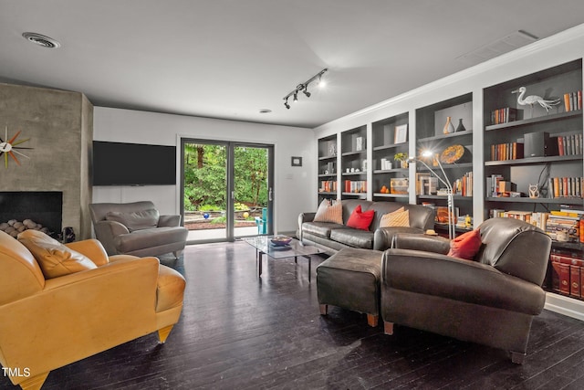 living area with built in shelves, wood-type flooring, a large fireplace, and visible vents