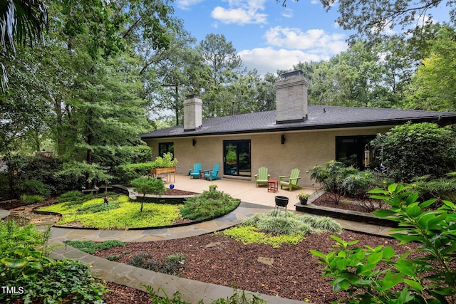 rear view of house with a patio area, brick siding, and a chimney