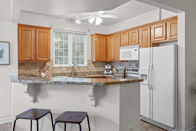 kitchen featuring a breakfast bar, backsplash, white appliances, stone countertops, and ceiling fan