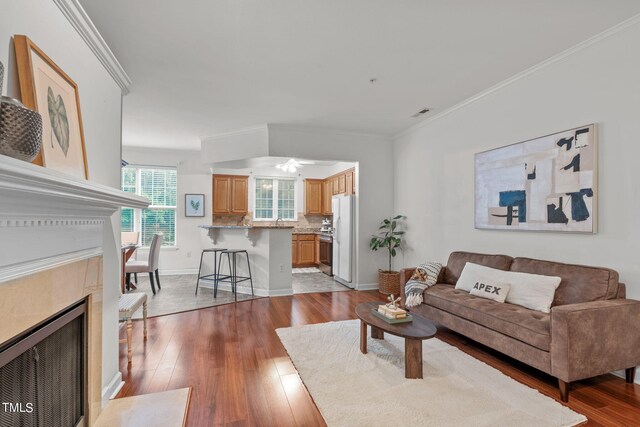 living room with crown molding, ceiling fan, a high end fireplace, and light hardwood / wood-style flooring