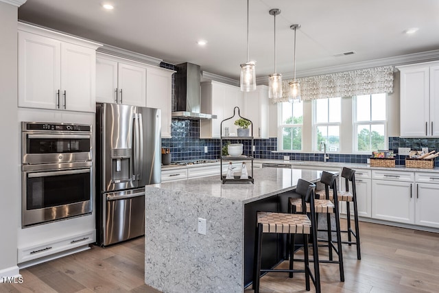 kitchen featuring white cabinets, appliances with stainless steel finishes, wall chimney range hood, and a kitchen island