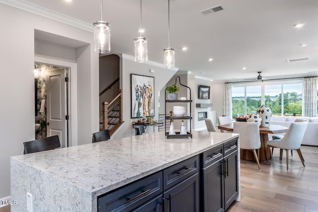 kitchen with light stone counters, a kitchen island, light wood-type flooring, decorative light fixtures, and ornamental molding