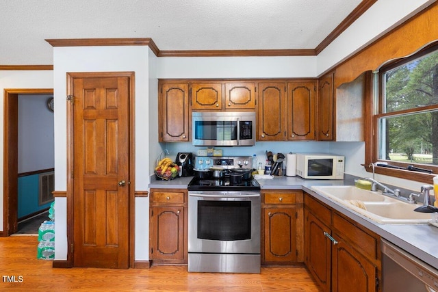 kitchen featuring light wood-type flooring, appliances with stainless steel finishes, crown molding, and sink