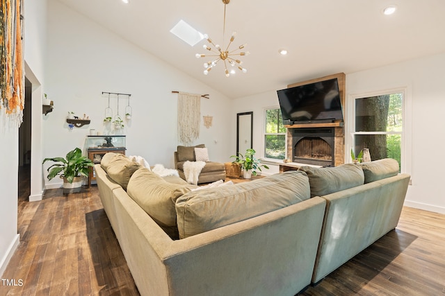 living room with a skylight, a chandelier, high vaulted ceiling, hardwood / wood-style flooring, and a fireplace