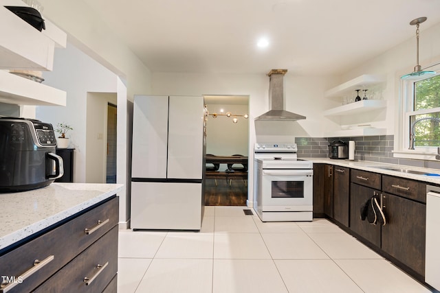 kitchen with wall chimney exhaust hood, white appliances, dark brown cabinetry, sink, and hanging light fixtures