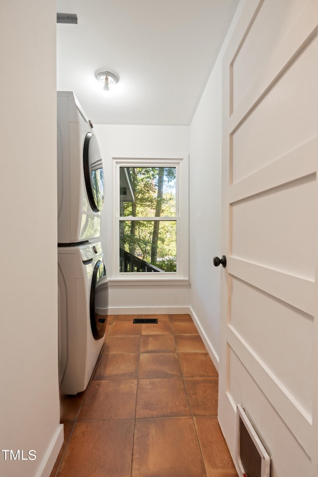 clothes washing area featuring stacked washer and dryer and dark tile patterned flooring