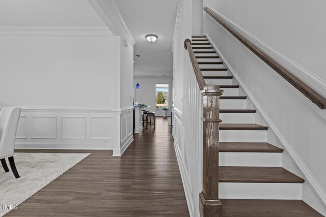 stairway with wood finished floors, a decorative wall, a wainscoted wall, and ornamental molding