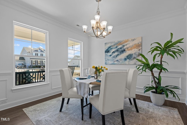 dining area featuring dark wood-style floors, a decorative wall, crown molding, and an inviting chandelier