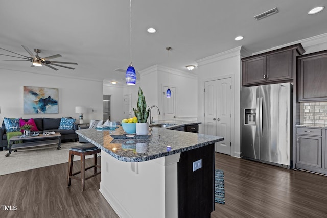 kitchen featuring dark brown cabinetry, an island with sink, a breakfast bar area, stainless steel fridge, and a sink