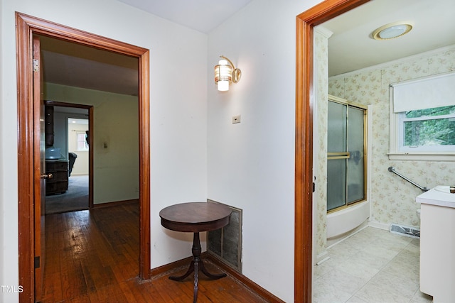 hallway with wood-type flooring, visible vents, baseboards, and wallpapered walls