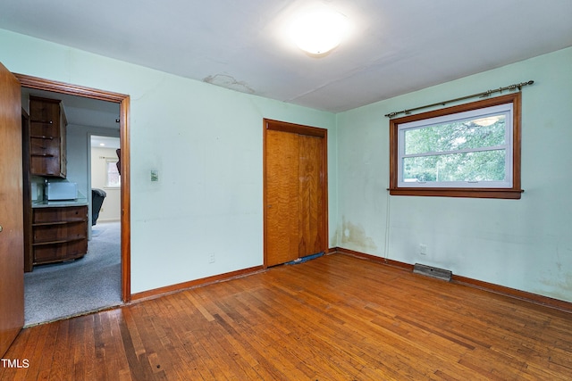 unfurnished room featuring baseboards, visible vents, and hardwood / wood-style floors