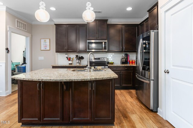 kitchen featuring hanging light fixtures, a center island with sink, backsplash, light hardwood / wood-style flooring, and appliances with stainless steel finishes