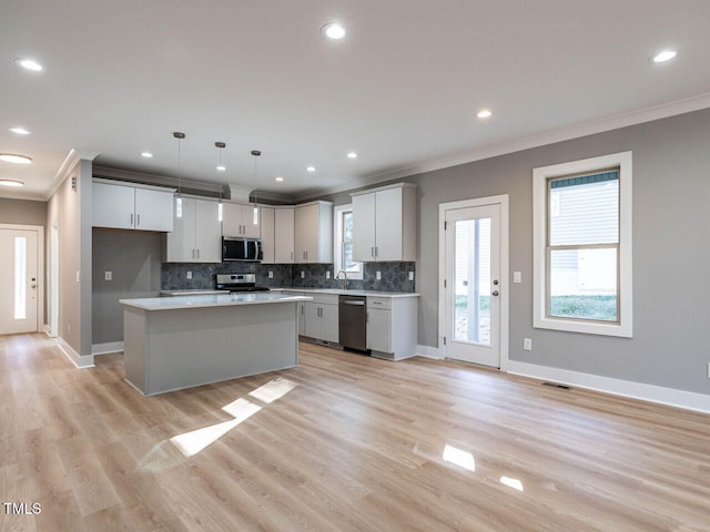 kitchen featuring appliances with stainless steel finishes, light wood-type flooring, a kitchen island, white cabinetry, and hanging light fixtures