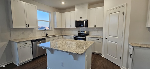 kitchen with stainless steel appliances, a kitchen island, sink, and white cabinets