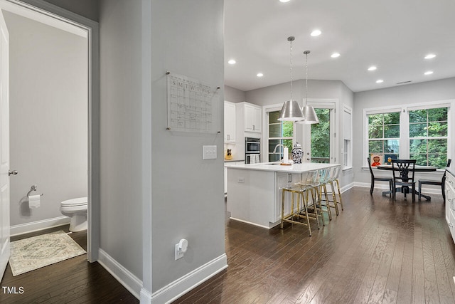 interior space with white cabinetry, a kitchen island, dark hardwood / wood-style flooring, pendant lighting, and a kitchen bar