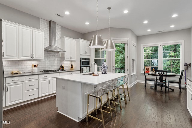 kitchen featuring hanging light fixtures, white cabinets, wall chimney exhaust hood, dark hardwood / wood-style flooring, and a kitchen island with sink