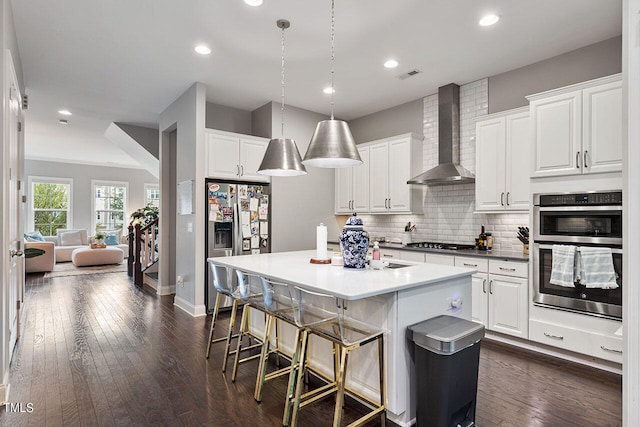 kitchen with decorative light fixtures, wall chimney range hood, stainless steel appliances, and white cabinets