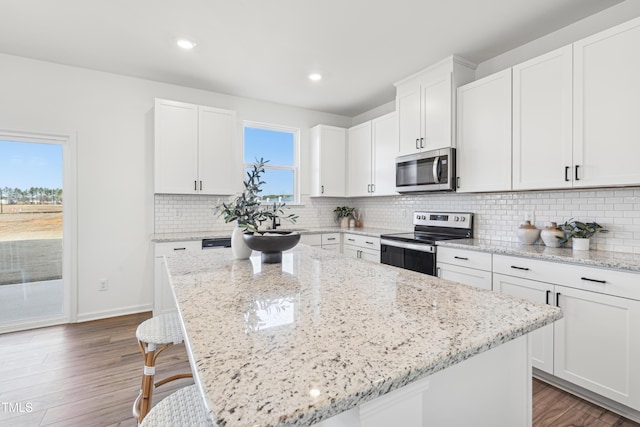 kitchen featuring white cabinets, stainless steel appliances, a kitchen island, and light stone counters