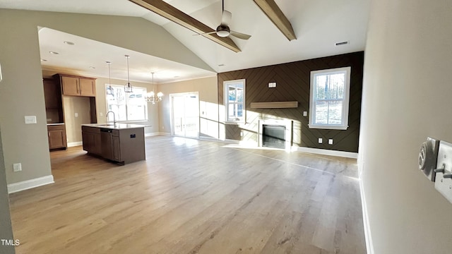 unfurnished living room with lofted ceiling with beams, light hardwood / wood-style flooring, plenty of natural light, a fireplace, and ceiling fan with notable chandelier