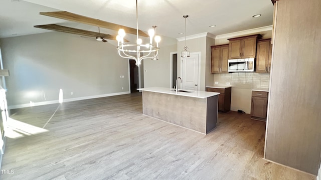 kitchen with backsplash, sink, pendant lighting, light hardwood / wood-style floors, and an island with sink