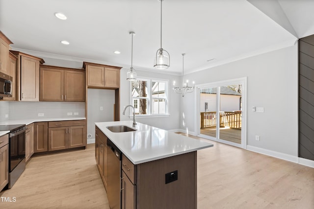 kitchen with sink, a kitchen island with sink, stainless steel appliances, ornamental molding, and decorative light fixtures