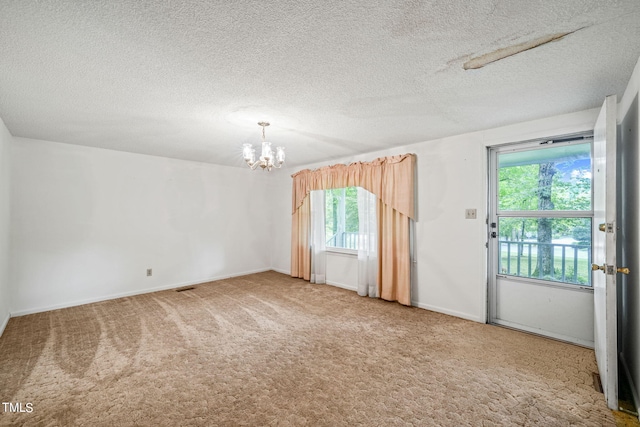 spare room featuring plenty of natural light, carpet, and an inviting chandelier