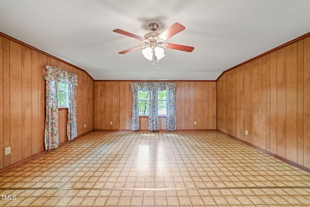 empty room featuring a textured ceiling, ceiling fan, and wood walls