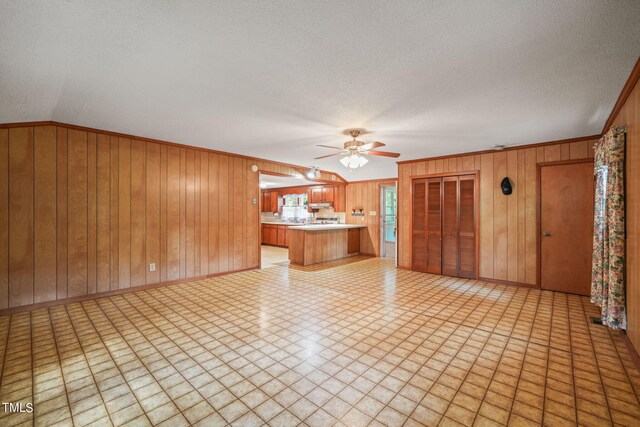 unfurnished living room with ceiling fan, wood walls, and a textured ceiling