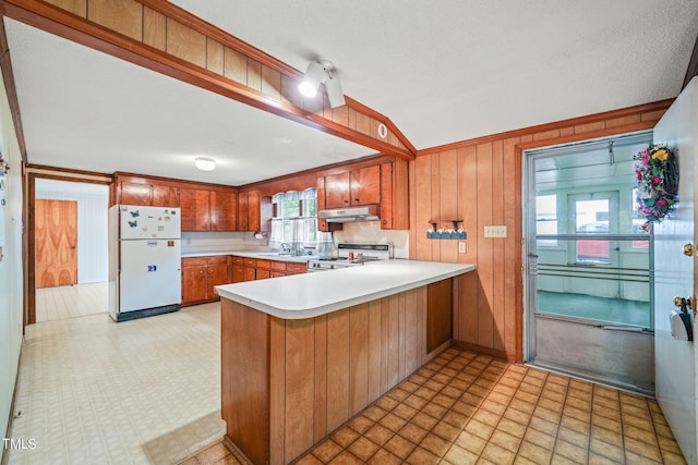 kitchen featuring stainless steel range oven, white refrigerator, sink, wood walls, and kitchen peninsula