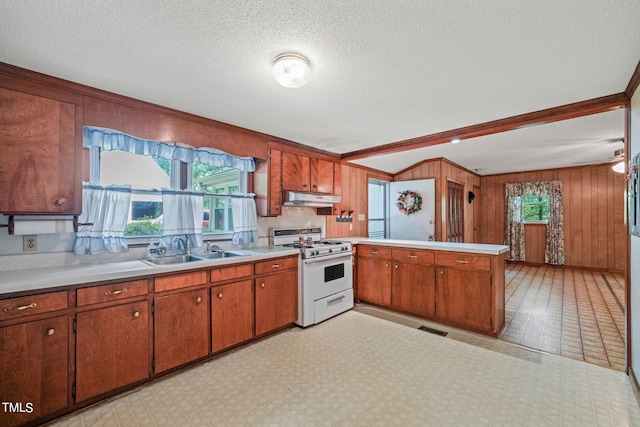 kitchen featuring a textured ceiling, sink, wood walls, kitchen peninsula, and white gas range oven