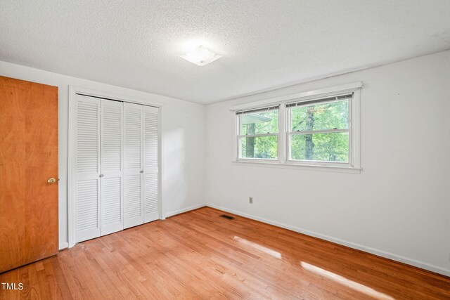 unfurnished bedroom featuring a textured ceiling, light hardwood / wood-style flooring, and a closet