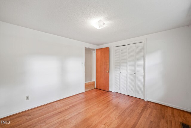 unfurnished bedroom featuring a closet, a textured ceiling, and light hardwood / wood-style flooring