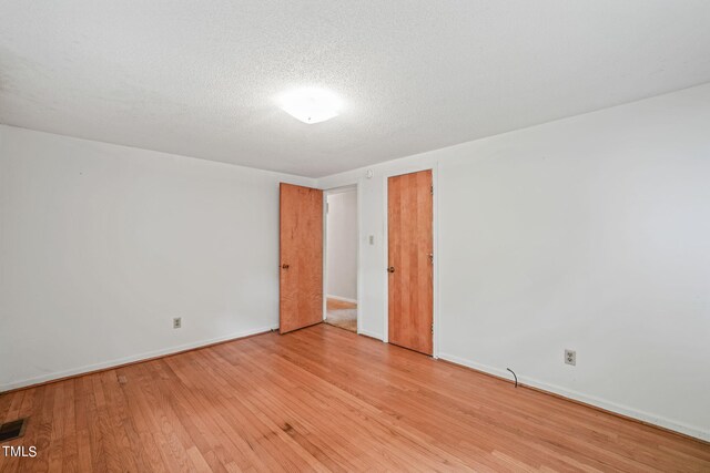 unfurnished room with light wood-type flooring and a textured ceiling