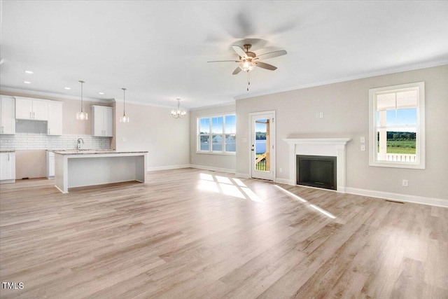 unfurnished living room featuring light wood-type flooring, ceiling fan with notable chandelier, and a wealth of natural light