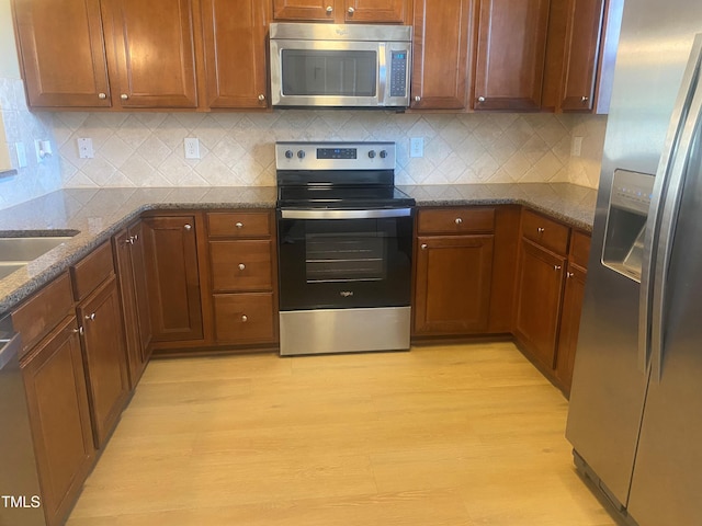 kitchen featuring tasteful backsplash, dark stone counters, light wood-type flooring, and appliances with stainless steel finishes