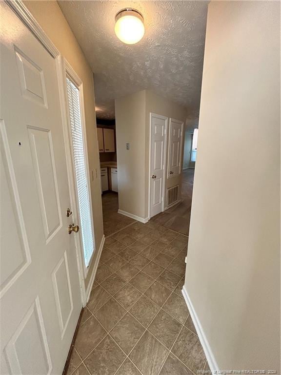 hall with a textured ceiling and tile patterned flooring