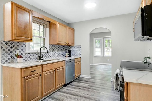 kitchen featuring decorative backsplash, light stone counters, stainless steel dishwasher, sink, and light hardwood / wood-style floors