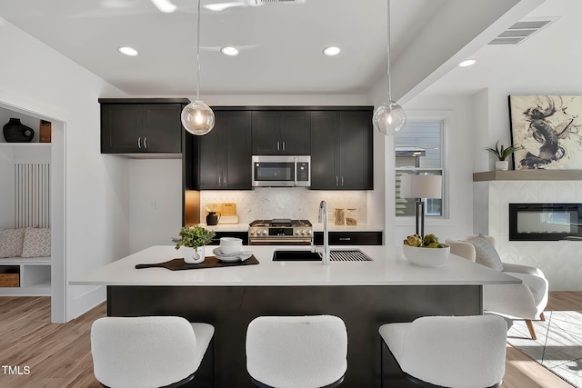 kitchen featuring pendant lighting, stainless steel appliances, a kitchen island with sink, and sink