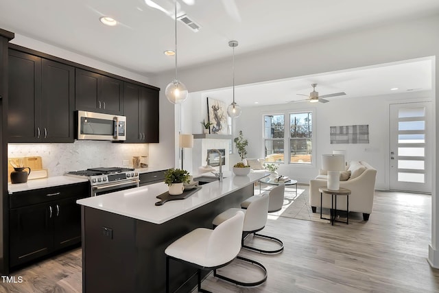 kitchen with pendant lighting, a center island with sink, light hardwood / wood-style flooring, ceiling fan, and stainless steel appliances