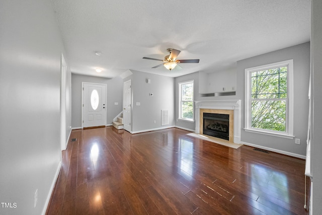 unfurnished living room with a textured ceiling, dark hardwood / wood-style flooring, ceiling fan, and a wealth of natural light