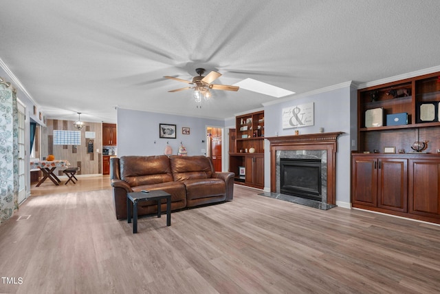 living room featuring ceiling fan, a high end fireplace, a textured ceiling, light wood-type flooring, and crown molding