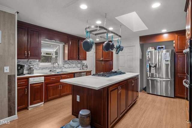 kitchen with a skylight, a textured ceiling, appliances with stainless steel finishes, a center island, and light hardwood / wood-style floors