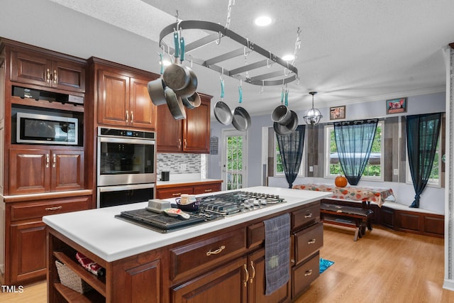 kitchen with a textured ceiling, a center island, light hardwood / wood-style flooring, stainless steel appliances, and backsplash